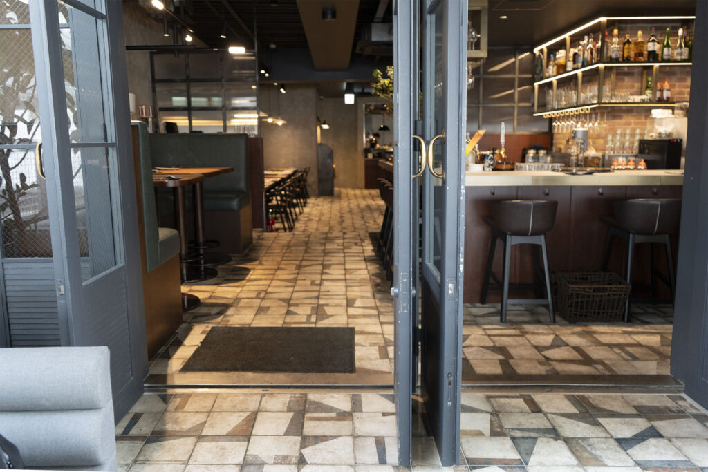 ガラス扉の入口から見た店内。BOTTEGA（PLAY）の床が奥のバーカウンターまで続く