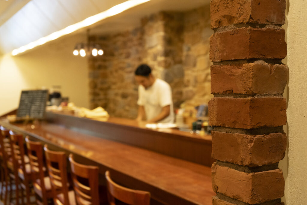 TRATTORIA ICIEIのカウンター席から見た店内。手前にブリック仕上げの柱、奥にRUS-1の石積み壁と厨房が続く