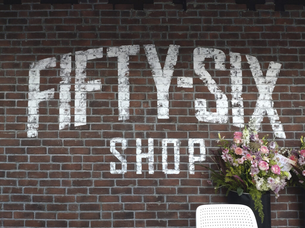 キャンブリック STANDARD STD-30 のレンガ調タイルの壁に描かれた FIFTY-SIX SHOP の白いロゴ。グレー目地のランダム張り